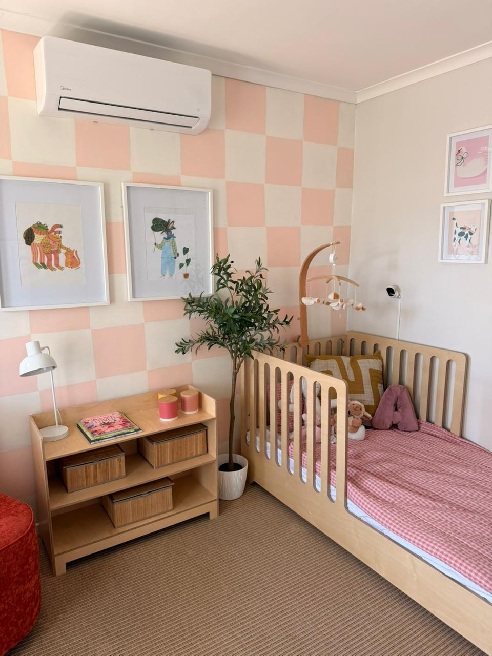Children's bedroom with checkered pink and white wall, wooden crib, and bookshelf.