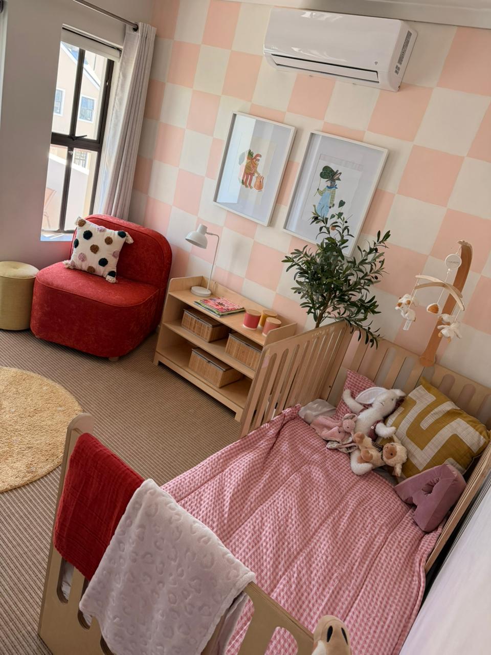 Children's bedroom with pink checkered wall, red chair, and wooden bed.