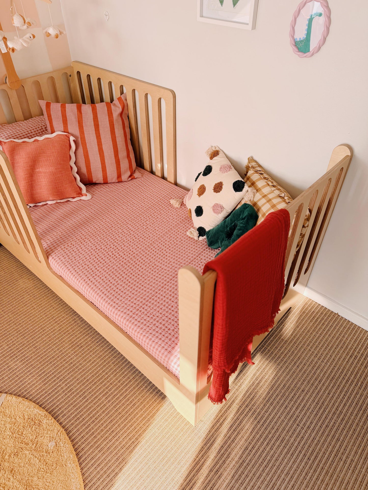 Children's bed with pink bedding, red blanket, and colorful pillows in a room.
