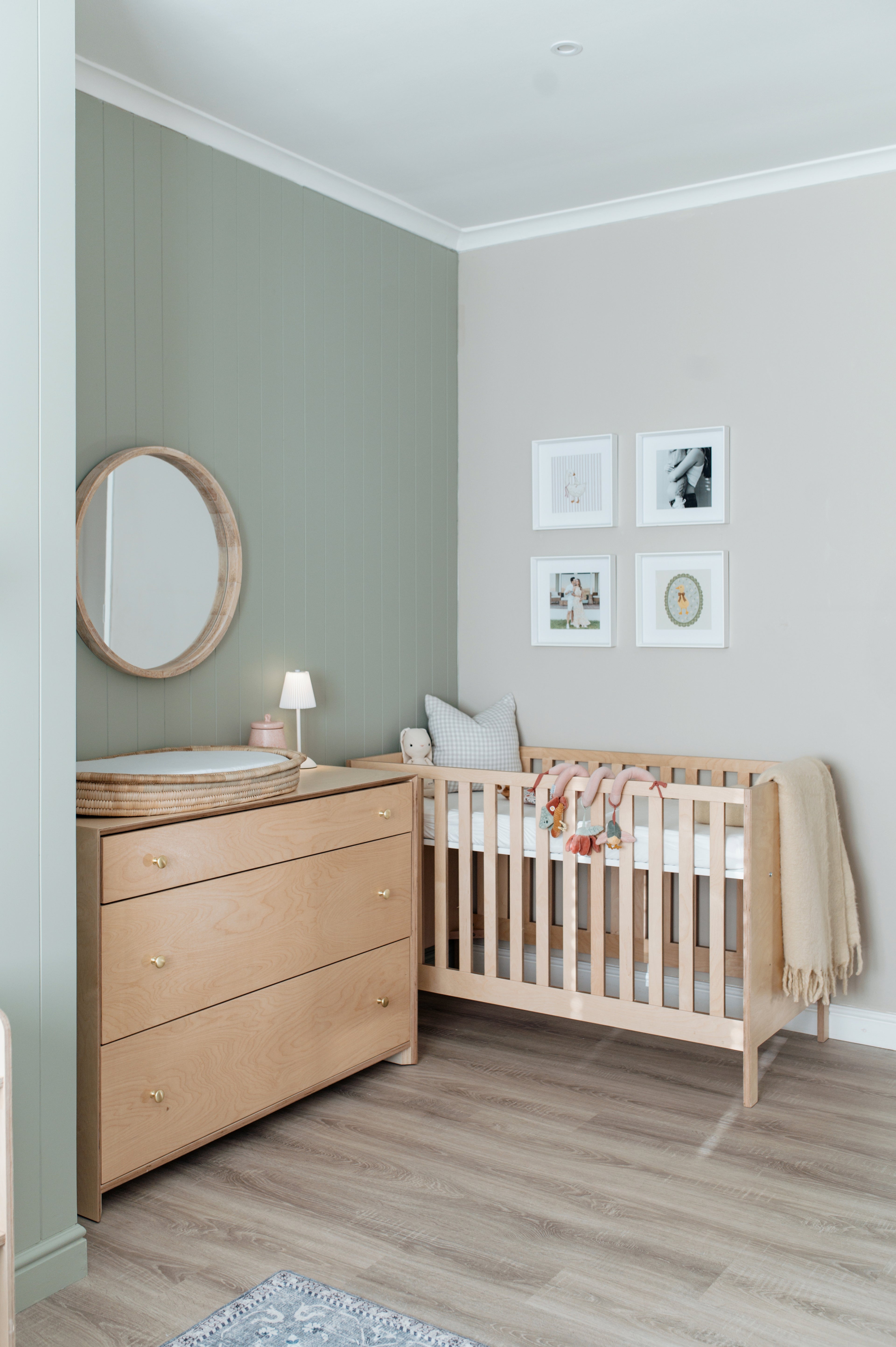 Nursery room with wooden crib and dresser against a light gray wall.