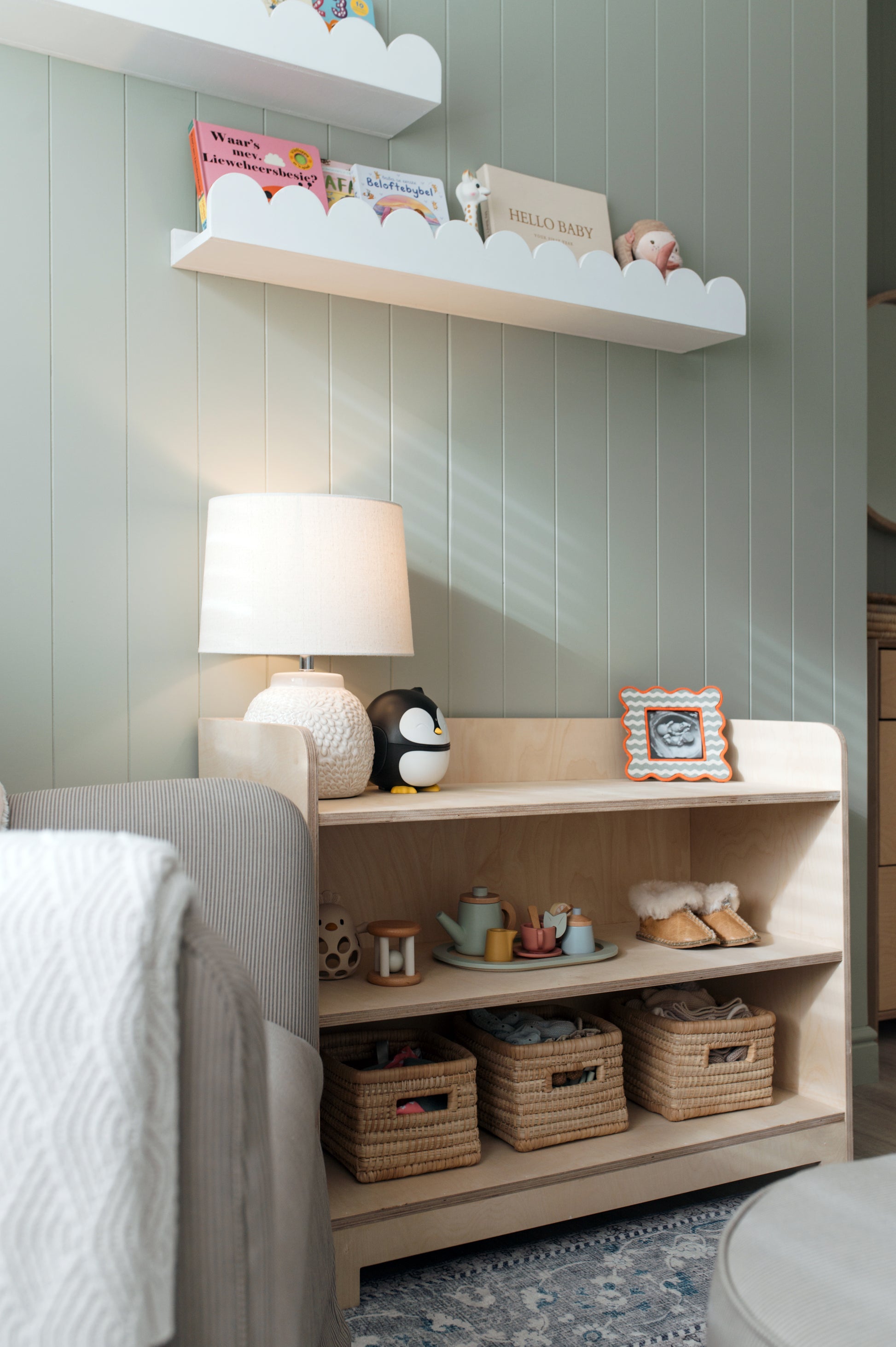 Nursery room with shelves, lamp, and toys against a light green wall.