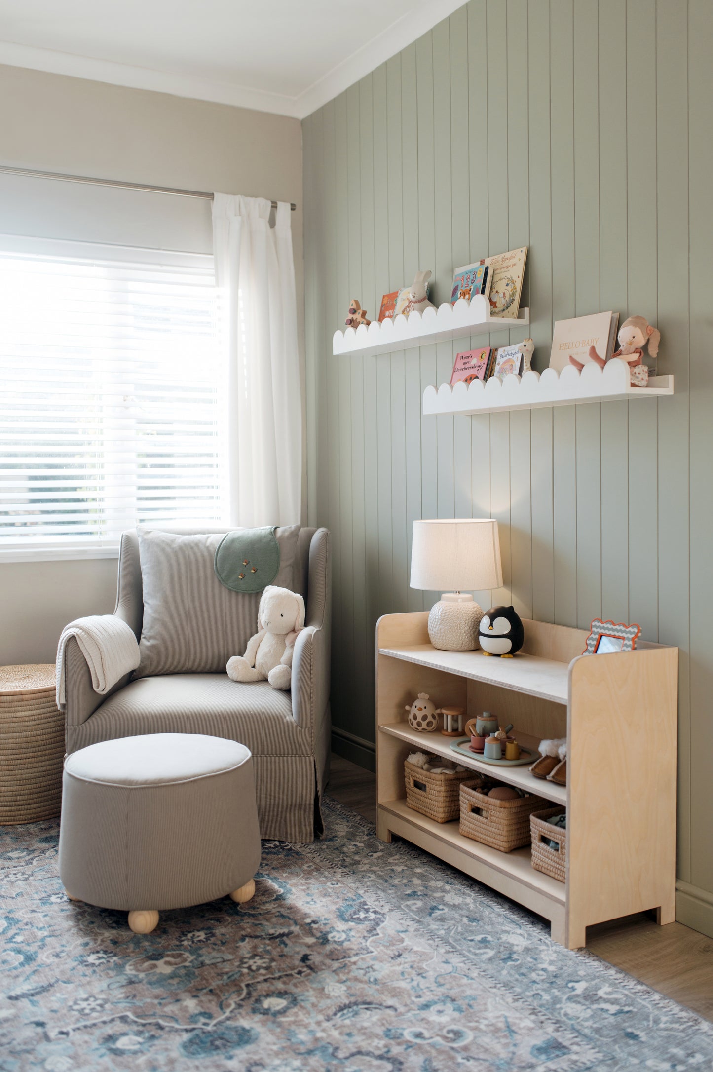 Nursery room with a chair, ottoman, and shelves with toys and decor.