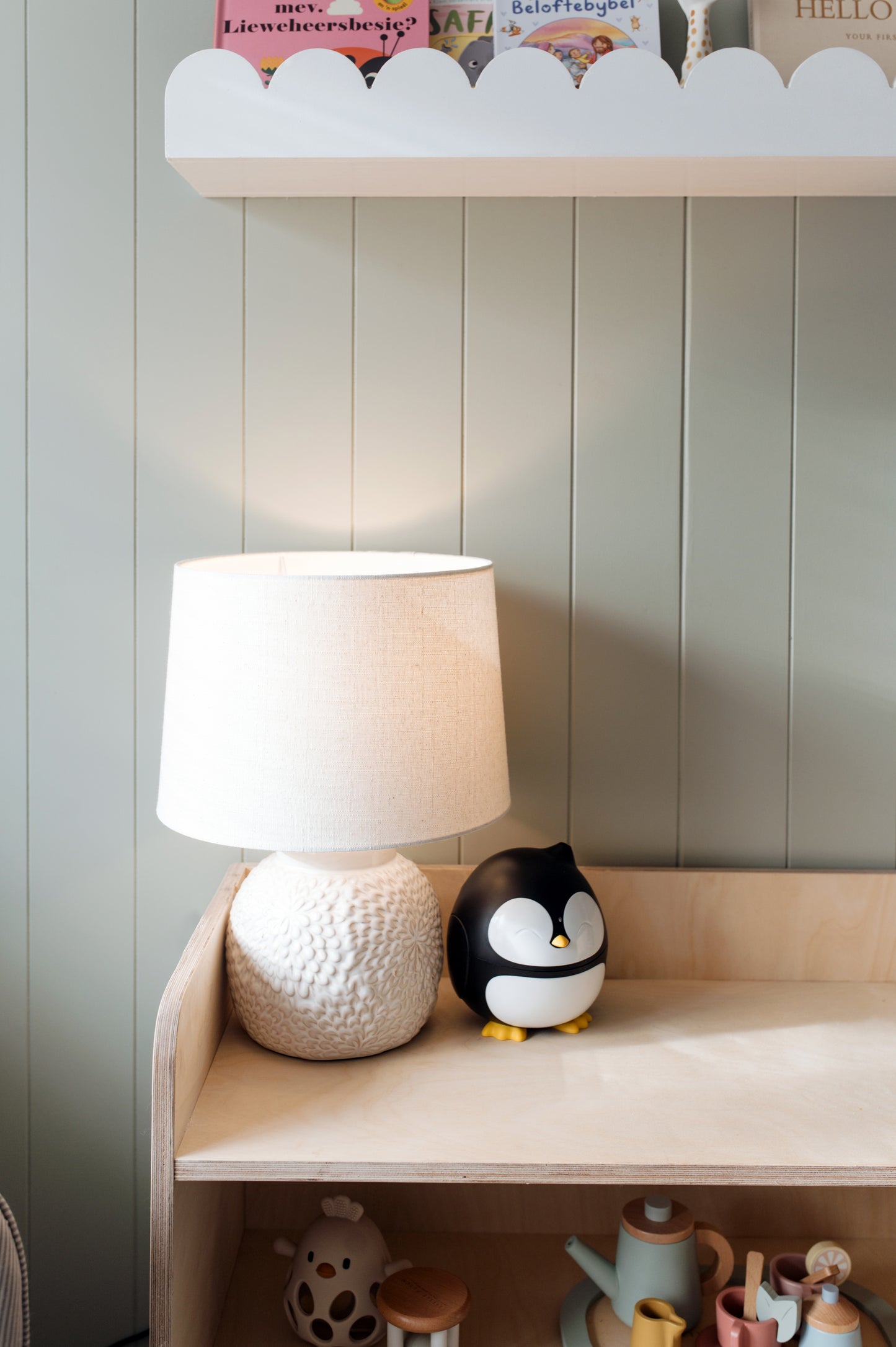 White lamp and penguin figurine on a wooden shelf against a light gray wall.