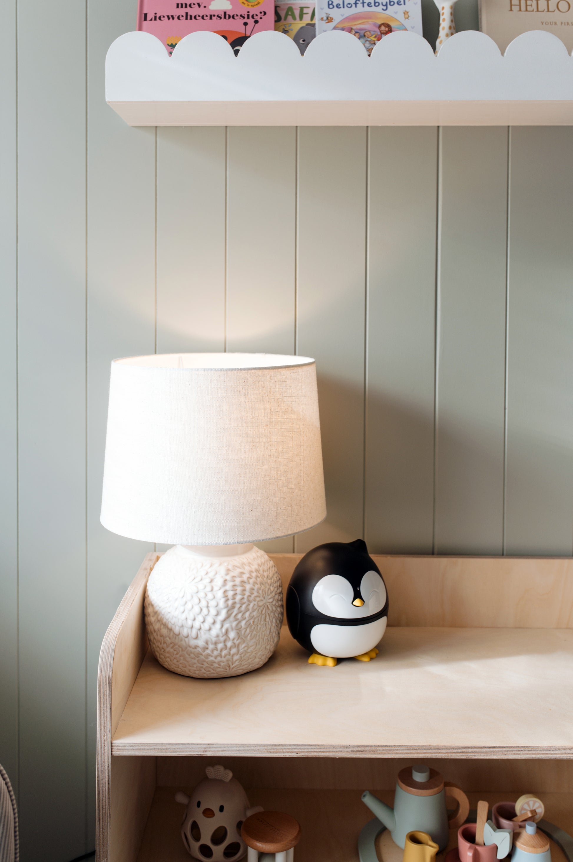White lamp and penguin figurine on a wooden shelf against a light gray wall.