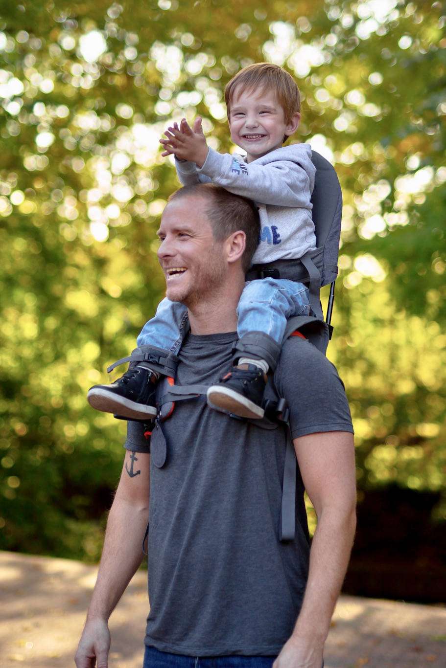 Happy child riding on parent's shoulders secured by the MiniMeis G5 Carrier