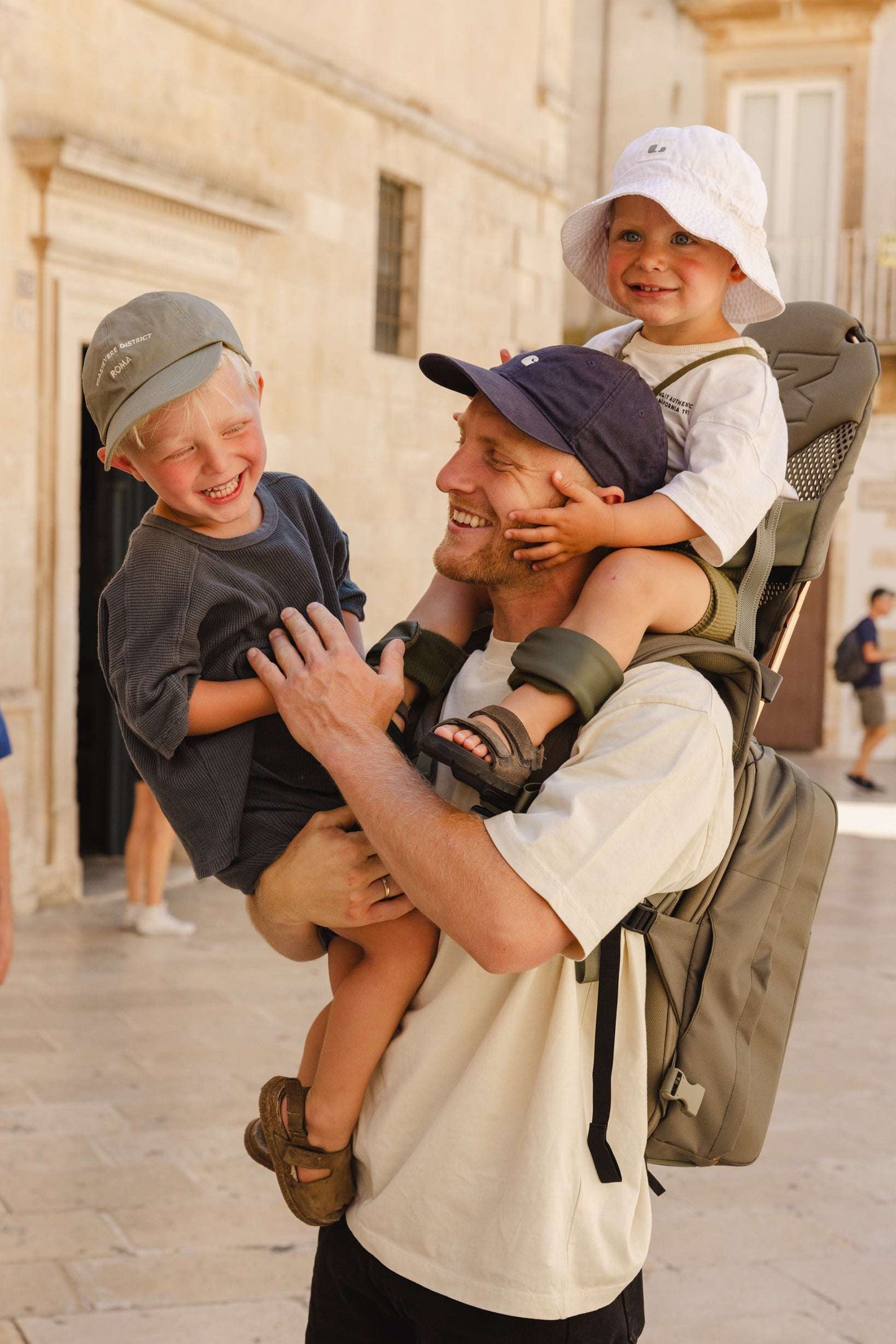 Happy child riding on parent's shoulders secured by the MiniMeis G5 Carrier